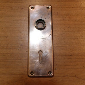 May include: A vintage copper door plate with a keyhole and a round hole for a door knob.