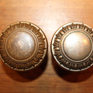 May include: Two antique brass door knobs with a decorative floral design around the edge.