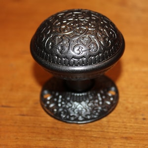 May include: A black metal door knob with an ornate design. The knob is round and has a decorative base.