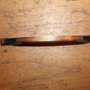 May include: A copper-toned drawer pull with a decorative grooved design.