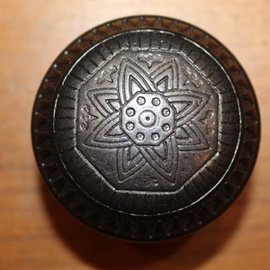 May include: A black, round, decorative knob with an intricate, carved design featuring a starburst pattern.