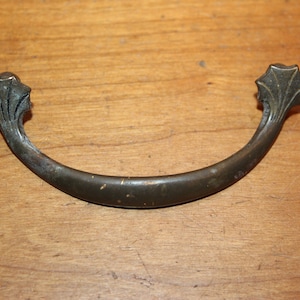 May include: A vintage,  bronze-colored,  metal drawer pull with a curved shape and decorative,  leaf-like ends.