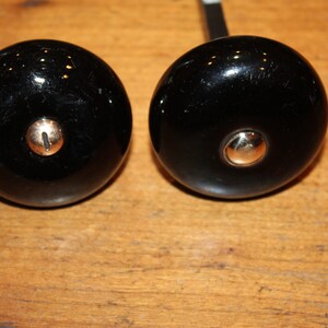 May include: Two black ceramic door knobs with gold accents. The knobs are round and have a single screw hole in the center.