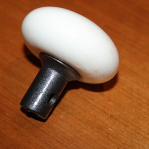 May include: White ceramic door knob with a black metal stem. The knob is round and has a smooth surface.