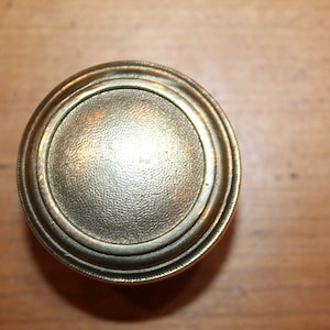 May include: A round, brass door knob with a smooth, textured surface and a raised, concentric ring design.