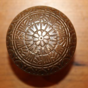 May include: A vintage brass door knob with an intricate, circular design. The knob features a central flower motif surrounded by repeating geometric patterns.