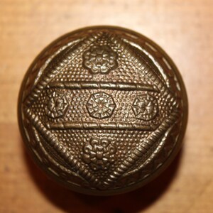 May include: A round, ornate, brass door knob with a geometric pattern and floral accents.