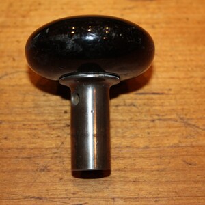 May include: Black ceramic knob with a silver metal stem. The knob is round and has a smooth surface. The stem is cylindrical and has a hole in the center.