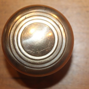 May include: A round, brass door knob with concentric circles.