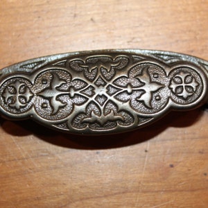 May include: A vintage-style, ornate, metal drawer pull with a decorative, floral design. The pull is a dark, aged bronze color.