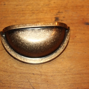 May include: A gold-toned metal cabinet pull with a rounded, cup-shaped design.