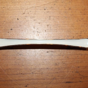 May include: A white ceramic cabinet pull with a gold trim. The pull is curved and has a simple design.