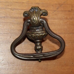 May include: A vintage brass drawer pull with a decorative floral design and a ring handle.
