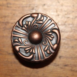 May include: A decorative cabinet knob with a copper finish and intricate floral design.