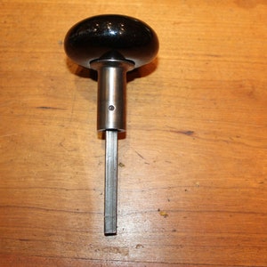 May include: Black ceramic door knob with a silver metal shaft and a square end.