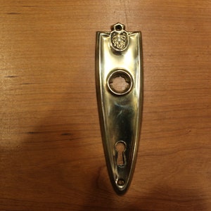 May include: A gold-toned door plate with a keyhole and a decorative design at the top.