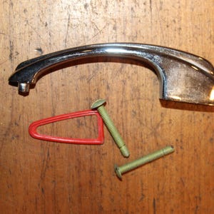 May include: A chrome door handle with a curved design. It comes with two screws and a red plastic washer.
