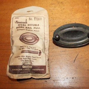 May include: Antique English finish oval double bore bail pull cabinet hardware with a screw and packaging. The packaging includes the product number ET860 and the brand name Amerock.