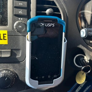 May include: A USPS handheld device in a car mount. The device is black and blue with the USPS logo. A yellow sticker with the word "POSSIBLE" is on the dashboard.