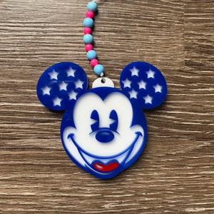 May include: A blue and white Mickey Mouse character with stars on the ears. The character is hanging from a string of pink and blue beads.