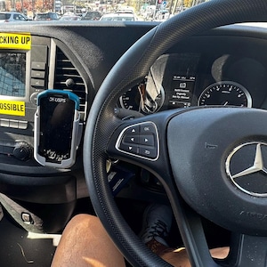 Puede incluir: Interior de un veh&iacute;culo con volante negro y logotipo de Mercedes-Benz. Un dispositivo GPS est&aacute; montado cerca de la pantalla de infoentretenimiento. Pegatinas amarillas con los textos "AVOID BACKING UP" y "WHENEVER POSSIBLE".