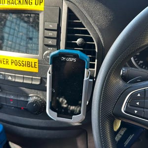 Puede incluir: Interior de un veh&iacute;culo con salpicadero y dispositivo USPS montado. Pegatinas amarillas con el texto "AVOID BACKING UP" y "WHENEVER POSSIBLE". Tambi&eacute;n se ven el volante y parte del salpicadero.