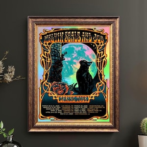 May include: Framed art print featuring a black cat silhouette against a colorful moon and rose. The artwork has gold ornate borders and includes tour dates for 2025. The print is in a brown wooden frame.