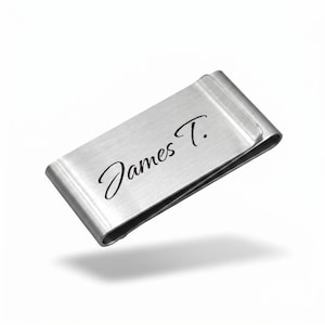 May include: A silver-colored money clip with the name "James T." elegantly scripted on the front. The clip has a brushed metal finish and a curved design for holding bills securely. The background is plain white.