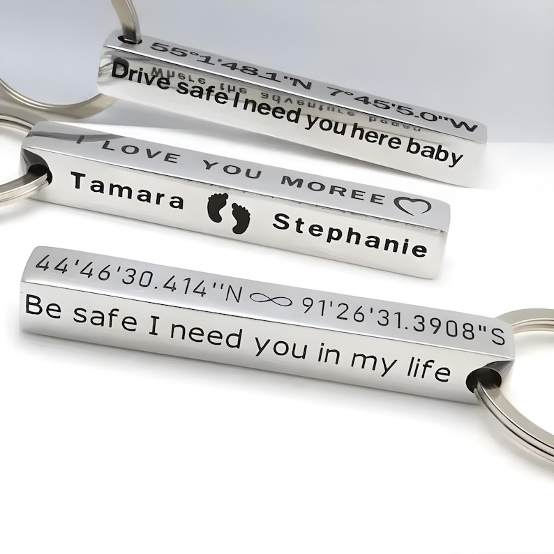 May include: Three silver rectangular keychains with engraved text. The keychains have phrases like "Drive safe I need you here baby" and "Be safe I need you in my life". One keychain has the name "Tamara" and footprints.