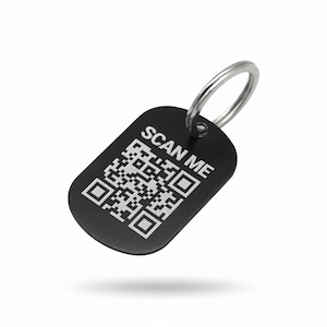 Könnte beinhalten: Schwarzer rechteckiger Schlüsselanhänger mit silbernem Schlüsselring. Der Schlüsselanhänger hat einen QR-Code und die weißen Worte "SCAN ME". Der Schlüsselanhänger ist leicht nach rechts geneigt, vor weißem Hintergrund.