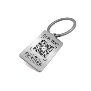 May include: A silver rectangular keychain with a QR code and the text "DEIN TEXT" at the top. The bottom of the keychain has the text "GRAVURENKING" and "INDIVIDUELLE LASERGRAVUREN". The keychain has a silver ring.