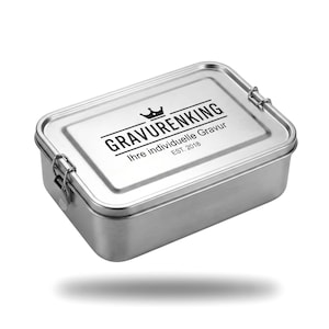 Könnte beinhalten: Eine rechteckige Edelstahl-Lunchbox mit einem Klappdeckel. Auf dem Deckel steht in schwarzer Schrift "GRAVURENKING" über "Ihre individuelle Gravur EST. 2018". Die Lunchbox hat eine glänzende, metallische Oberfläche.