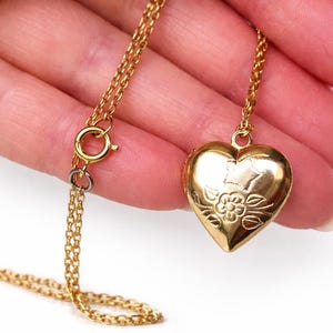 Può includere: Una collana con pendente a forma di cuore dorato. Il medaglione presenta un motivo floreale e una stella. La catena e la chiusura sono anch'esse dorate. La collana è un gioiello delicato.