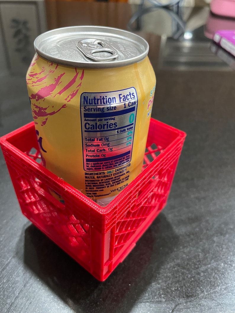 Puede incluir: Una lata amarilla con tapa plateada se encuentra dentro de una peque&ntilde;a caja de pl&aacute;stico roja. La lata tiene una etiqueta de informaci&oacute;n nutricional visible. La caja es cuadrada con un dise&ntilde;o de celos&iacute;a.