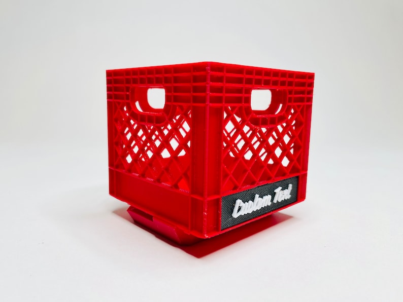 Puede incluir: Una caja de pl&aacute;stico roja con forma rectangular y dise&ntilde;o de celos&iacute;a. La caja tiene dos grandes aberturas para las asas en los laterales. Una etiqueta negra con la inscripci&oacute;n "Custom Text" en blanco est&aacute; adherida en la parte delantera.