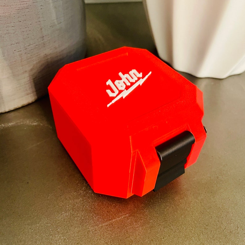 May include: A bright red, rectangular storage case with a black latch. The case has the word "John" printed in white on the top.