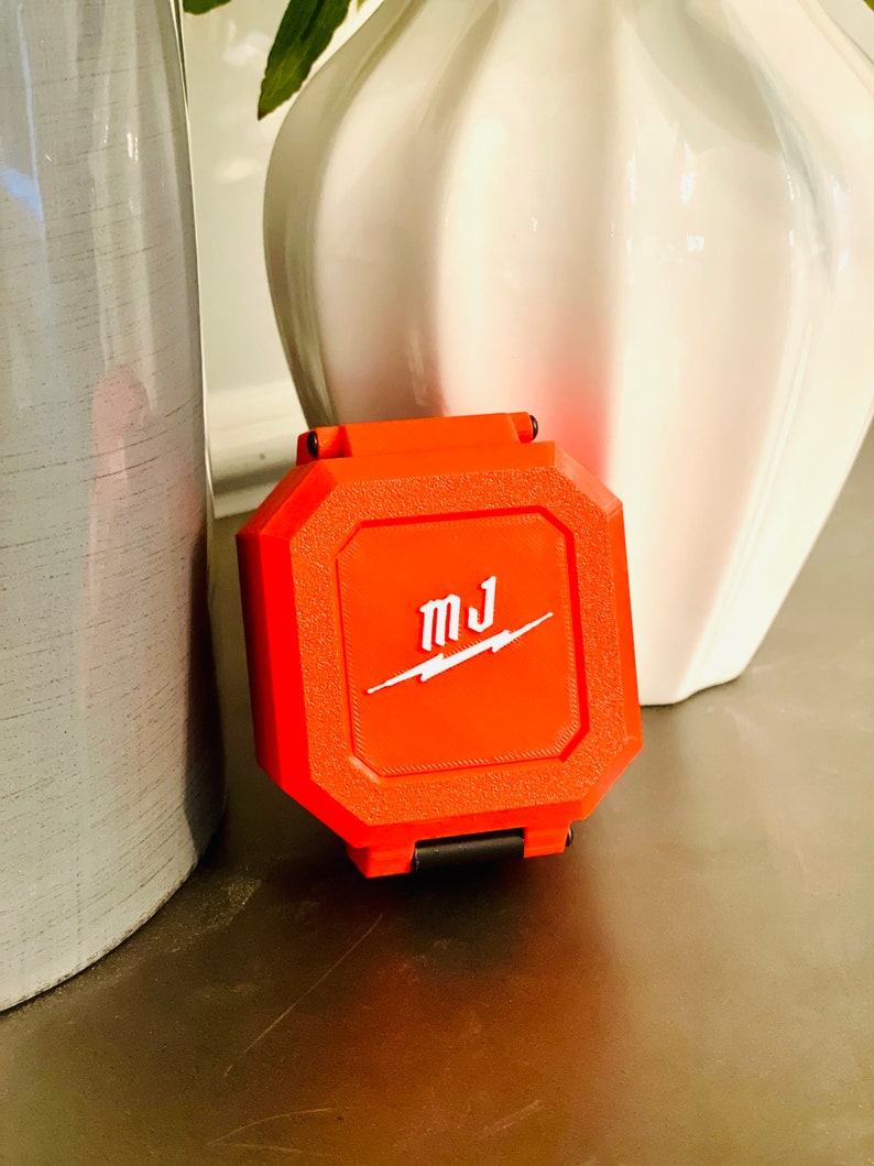 May include: A bright orange, octagonal-shaped case with a black latch. The case has the letters "MJ" and a lightning bolt logo in white.