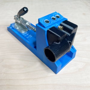 May include: A blue and black woodworking jig with a clamp and a drill guide. The jig has a depth gauge marked in 1/2 inch increments. The drill guide has three holes.