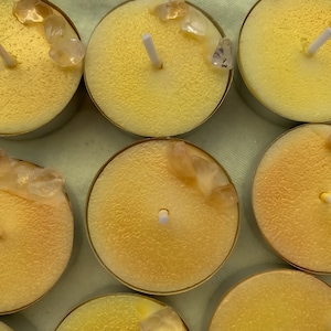 May include: Eight yellow tea light candles with small clear crystals on top. The candles are in a circular shape and have a small wick in the center.