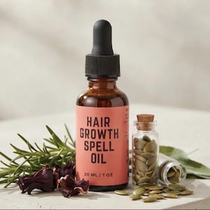 May include: An amber glass dropper bottle labelled HAIR GROWTH SPELL OIL 30 ML / 1 OZ with a black dropper cap. Beside it sits a small clear glass vial filled with pumpkin seeds, a sprig of fresh rosemary, and dried dark red hibiscus flowers.