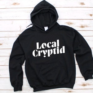 May include: Black hooded sweatshirt with white text that reads "Local Cryptid".
