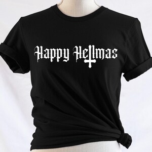 以下が含まれることがあります： 黒いTシャツ、袖は折り返されています。前面には、ゴシック体の白い文字で「Happy Hellmas」と十字のシンボルがプリントされています。柔らかい素材でできており、裾に結び目があります。