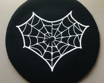 Könnte beinhalten: Eine schwarze Baskenmütze mit einem weißen Spinnennetz-Design.