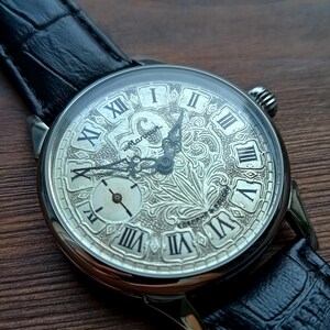 Puede incluir: Reloj de bolsillo plateado con una esfera grabada detallada con n&uacute;meros romanos y una peque&ntilde;a subesfera. El reloj tiene una correa de cuero negro y un dise&ntilde;o ornamentado. Un reloj cl&aacute;sico.