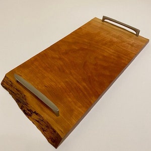 Op de afbeelding: Een rechthoekige houten dienblad met een natuurlijke houten afwerking en twee zilveren metalen handvatten. Het dienblad heeft aan &eacute;&eacute;n kant een levende rand.