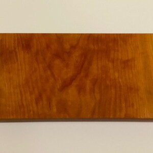 Op de afbeelding: Een rechthoekig houten bord met een natuurlijke houtnerf afwerking. Het bord heeft een licht ruwe, onafgewerkte rand en vier kleine gaten die in het oppervlak zijn geboord.