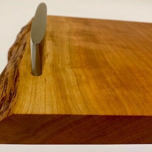 Op de afbeelding: Een houten dienblad met een natuurlijke houten afwerking en een zilveren metalen handvat. Het dienblad heeft een live edge-ontwerp en is perfect om eten of drinken te serveren.
