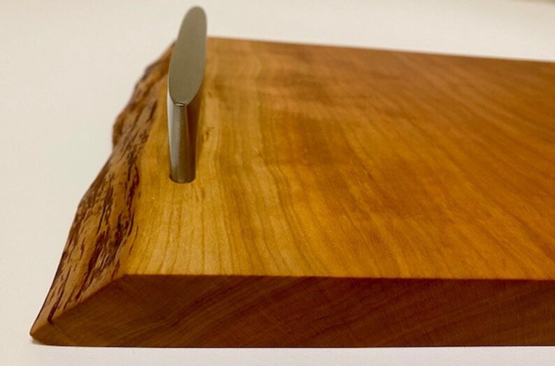 Op de afbeelding: Een houten dienblad met een natuurlijke houten afwerking en een zilveren metalen handvat. Het dienblad heeft een live edge-ontwerp en is perfect om eten of drinken te serveren.