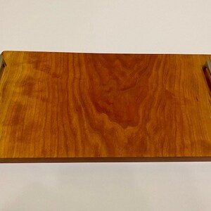Op de afbeelding: Een rechthoekige houten dienblad met een natuurlijke houten afwerking en twee metalen handvatten. Het dienblad heeft een live edge-ontwerp.
