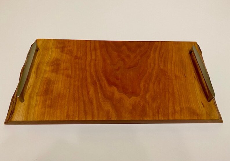 Op de afbeelding: Een rechthoekige houten dienblad met een natuurlijke houten afwerking en twee metalen handvatten. Het dienblad heeft een live edge-ontwerp.